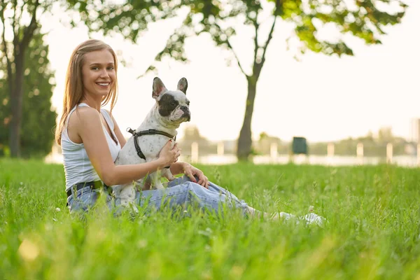 Smiling woman with french bulldog on grass.