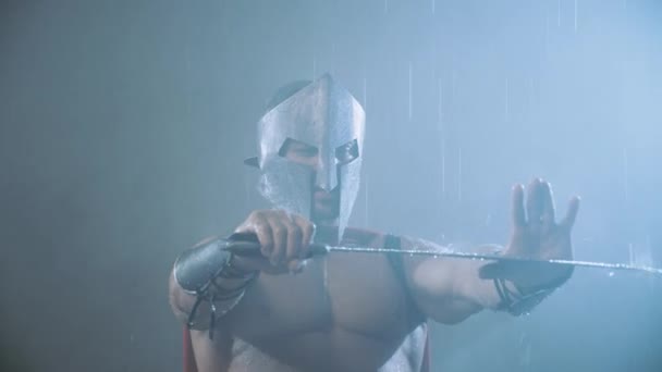 Espartano muscular segurando lâmina no polegar sob chuva. — Vídeo de Stock