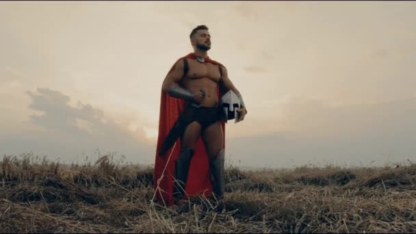 Handsome spartan posing in dry field, sunset. — Stock Video