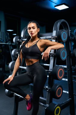 Spor salonunda halterlerin yanında poz veren sağlıklı bir kadın..