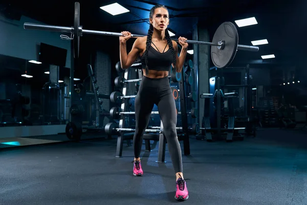 Female bodybuilder doing lunges using barbell in gym.