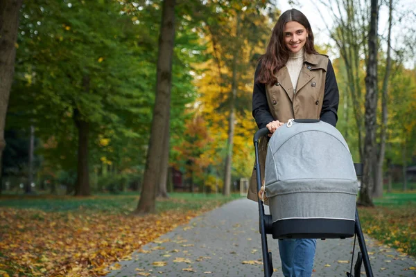 Bir kadın kameraya bakıyor ve yeni doğmuş bir bebekle bebek arabasını tutuyor..