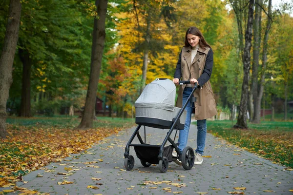 Woman spends time outdoors with baby in gray stroller. — Stock Photo, Image