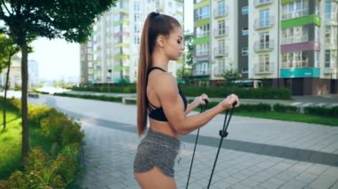 Spor kadını bisepsi eğitirken açık havada elastik halat bandı kullanıyor..