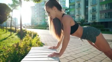 Dişi sporcu açık hava tezgahı kullanarak şınav çekiyor..