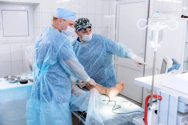 Un team di medici in sala operatoria conduce procedure mediche. I chirurghi in indumenti sterili lavorano in ospedale. Attrezzature mediche in clinica . — Foto Stock
