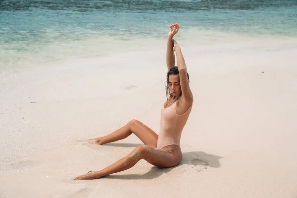 Menina incrível com corpo sexy está envolvida na aptidão na praia de areia branca. Jovens mulheres de maiô tomando banho de sol em férias de verão no exterior. Modelo encantador em uma ilha deserta. — Fotografia de Stock