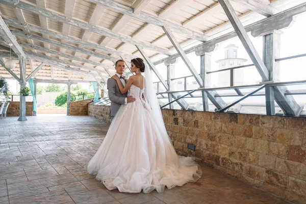 Gerade verheiratete Paar von schönen Bräutigam in einem grauen Business-Anzug und eine Braut in einem luxuriösen weißen Kleid mit Schleier mit erstaunlichem Haarschnitt. Brautpaar am Hochzeitstag. — Stockfoto