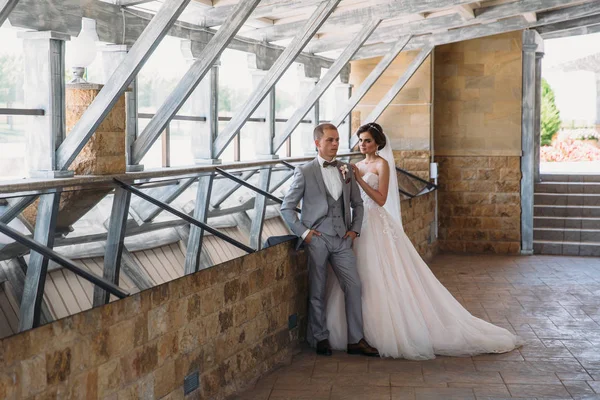 Gerade verheiratete Paar von schönen Bräutigam in einem grauen Business-Anzug und eine Braut in einem luxuriösen weißen Kleid mit Schleier mit erstaunlichem Haarschnitt. Brautpaar am Hochzeitstag. — Stockfoto