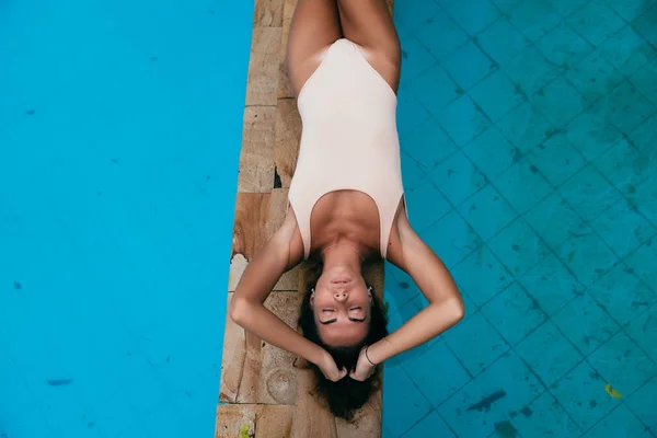 Una modelo con un bronceado sexy se relaja cerca de las piscinas. Hermosa cara y cuerpo de una joven en traje de baño. Vista desde arriba . — Foto de Stock