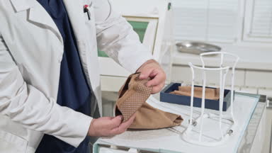 Beyaz bir tıbbi elbise ile bir doktor ameliyat öncesi kompresyon çorapları hazırlar. Hastanede ameliyat odasında belgesine bakın. Phlebology ve varis tedavisinde.