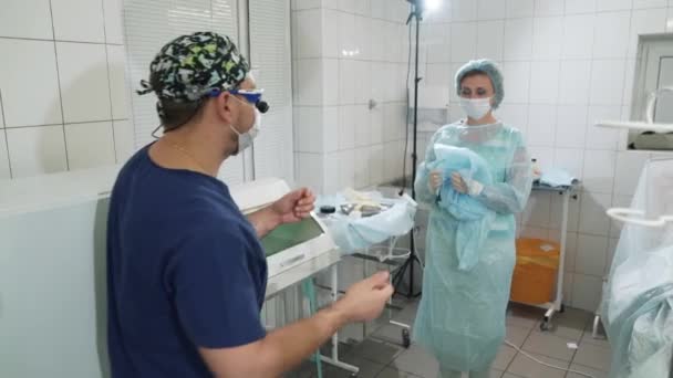 Lekarz wchodzi na salę operacyjną. Pielęgniarka pomaga ubrać suknię lekarzy w sali operacyjnej. Przygotowanie do zabiegu. Sali operacyjnej w szpitalu. Pielęgniarka i chirurg zaczynają się dla — Wideo stockowe