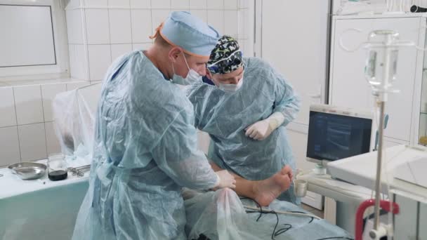 Les phlébologues opèrent les veines. Le patient avec des varices est venu à l'opération. Les médecins font des ultrasons sur la table d'opération. Les spécialistes ne travaillent pour enlever les varices sur leurs — Video