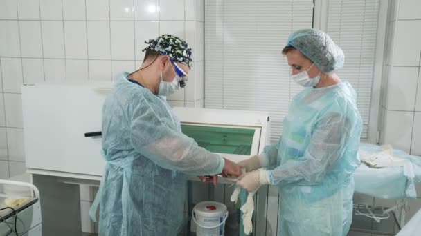 A enfermeira ajuda o cirurgião a vestir um vestido estéril e luvas. Os médicos estão se preparando para a cirurgia no departamento cirúrgico do hospital. O médico vai operar o paciente. O — Vídeo de Stock