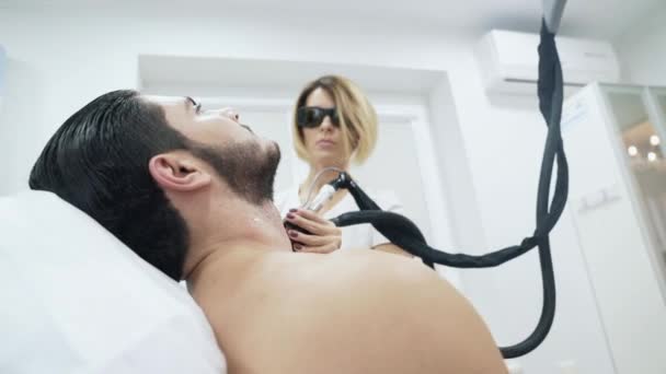 En cosmetología, se realiza un procedimiento de depilación láser. El médico conduce a los hombres alrededor del cuello del aparato para la depilación. El dispositivo con la ayuda de brotes mata el folículo piloso — Vídeo de stock