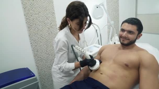 Косметолог проводит процедуру РФ-лифтинга для мужчины. Врач руководит аппаратом, который нагревает кожу и стимулирует работу лактанов, вырабатывающих коллаген на проблемной области — стоковое видео