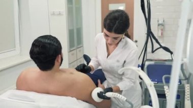 Atletik esmer onun makyajcısı bir yordam için geldi. Doktor istemci omzuna aygıt sürücüleri ve cilt tonu korumak için kaldırma yordamı Radyofrekans gerçekleştirir.