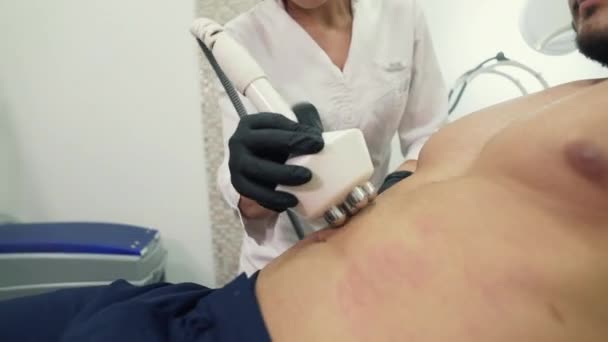 Крупный план врача, косметолога в перчатках, возглавляет устройство для РФ-лифтинга на животе клиента косметологической клиники. Процедура проведения радиочастотного подъема. Избавиться — стоковое видео