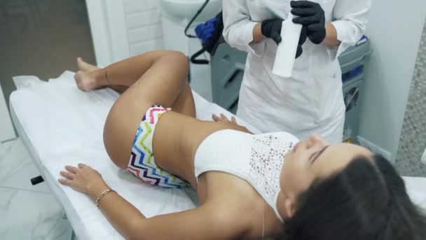 Una chica morena y delgada yace en la oficina de una esteticista. El cliente vino al RF-lifting. La chica quiere mejorar la calidad y el color de las caderas . — Vídeos de Stock