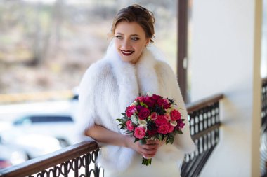 Gelin verandada, yün, ipek beyaz giyinmiş ve az önce geldi onu misafir gülümseyen duruyor. Kızı bir güzel kokulu buket çiçek tutuyor.