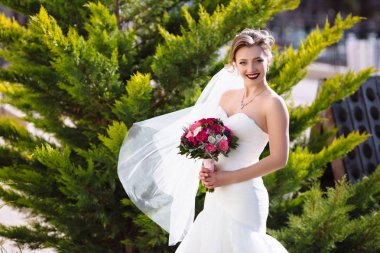 Sıkı bir gelinlik ince bir gelin Bahçedeki ağaçlar arka plan üzerinde duruyor. Ona elbise ve Pamuk yün rüzgar bora esiyor, kız neşeyle gülümsüyor ve an sahiptir.