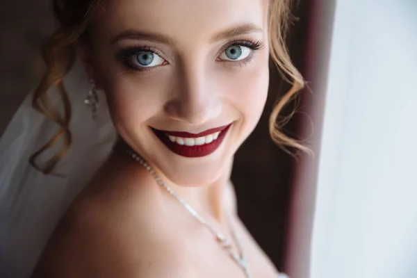 Primer plano de una rubia con rizos sonriendo dientes blancos como la nieve y labios oscuros. Una chica con grandes ojos hermosos grises. Mañana de la novia en el día de la boda, preparativos . —  Fotos de Stock