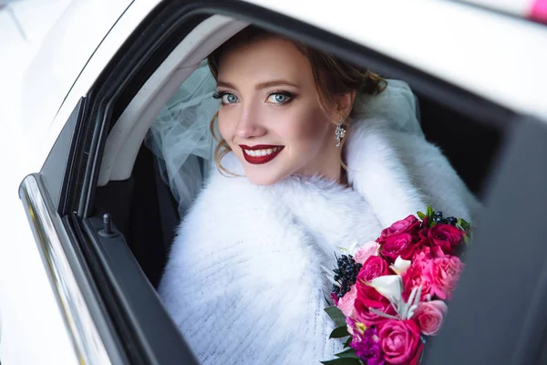 Dívka se spustil okna v autě a usmál se. Portrét detail modelu v bílém kožichu sedí na zadním sedadle auto s kyticí červených růží. — Stock fotografie