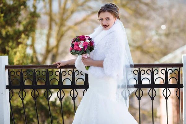 Eine schöne Braut posiert auf der Straße. Der Hochzeitstag ist Herbst, das Mädchen trägt einen weißen Nerzpelzmantel. Das Model lächelt strahlend. — Stockfoto