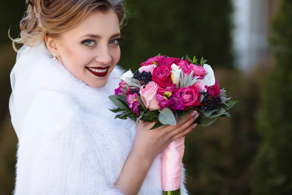 A noiva com cabelo loiro e francês manicure sorri e mostra seu lindo buquê. Vista próxima do rosto das noivas com olhos azuis, alegria do amor, humor do casamento . — Fotografia de Stock