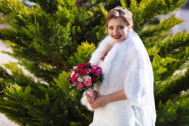 Gelin geniş gülümsüyor ve elinde bir buket gül, yeşil bahçe, arka plan karşı duran dudakları parlak ruj ile boyanır.