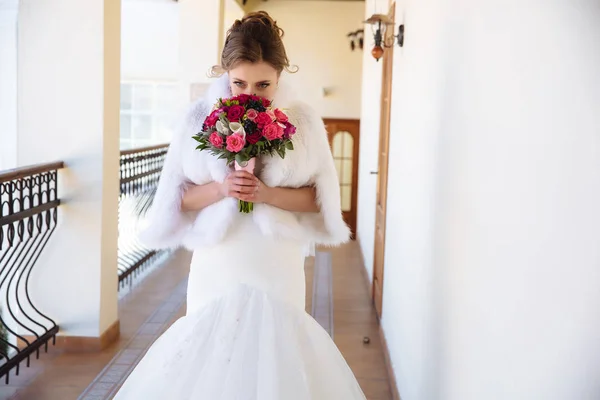 La novia con una hermosa capa blanca de lana está oliendo un ramo de rosas y disfrutando del aroma. La chica cubrió sus ojos de placer . —  Fotos de Stock