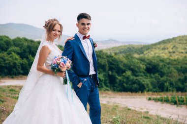 Gelin ve damat alan, üzüm bağları ve alanların zemin karşı durmak. Kız bir buket çiçek tutan ve güneşten biraz şaşı. Adam gülümsüyor ve elinde tutar