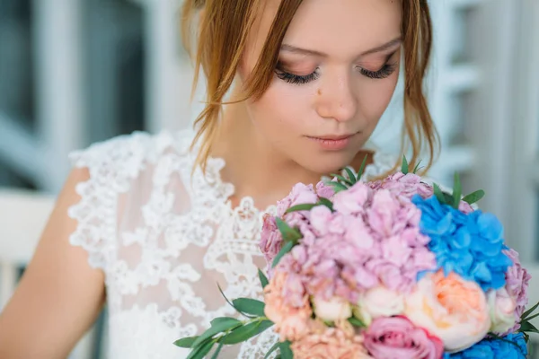 Um modelo com a maquilagem em cores naturais e grandes pestanas olha para um buquê de flores. Uma menina bonita inala o aroma de rosas e peônias . — Fotografia de Stock