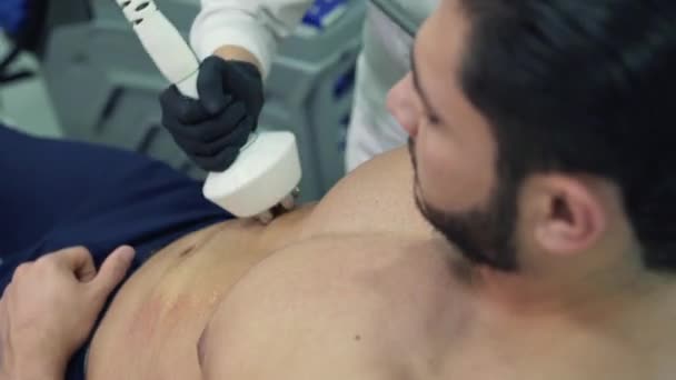 L'homme sportif aux cheveux foncés se trouve dans le fauteuil des cosmétologues et subit une procédure pour augmenter le flux sanguin dans l'abdomen. Le lifting RF est une procédure de cosmétologie indolore . — Video