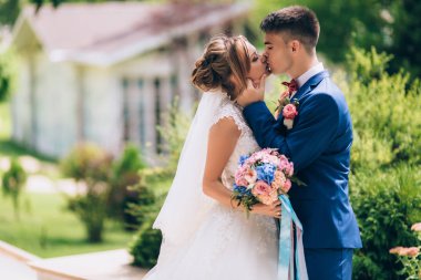 Nazik bir resmi arka plan yeşillik ve sütunlar ile bir bina için. Mavi elbiseli bir iş adamı yavaşça onu gelinlik kız basar. Yeni evliler öp. Hassasiyet ve ikisi arasında aşk