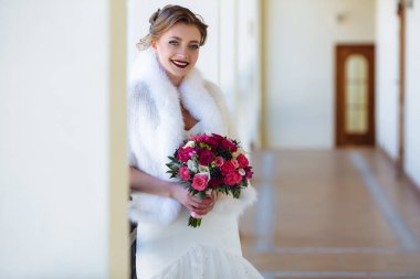 Akıllı bir kız beyaz elbise ve panço pencere ve gülümsüyor tarafından duruyor. Model pembe ve kırmızı gül buketi rujunu ile birlikte ellerini tutar.