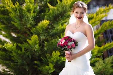 Dar elbiseli gelin yeşil bakire teşkil etmektedir ve güneş ışınlarının sahiptir. açıkça kız gülümsüyor, onun elinde pembe bir kurdele ile rewound çiçekler var..