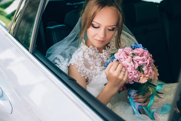 Bruden arrangerar noggrant blommor i buketten medan du sitter i bilen. Flickan tittar på bröllop bukett och tycker om sin älskade. — Stockfoto