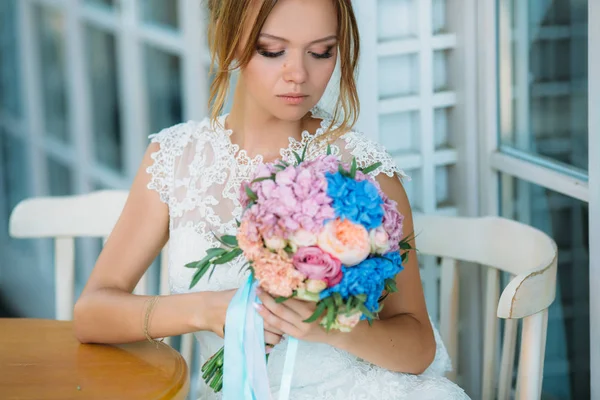 Den vackra bruden sänkte sina ögon till henne bukett av blommor. En flicka i en vit klänning beundrar rosor. — Stockfoto