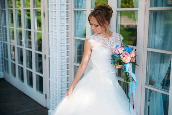 A noiva está olhando para o seu belo vestido branco no fundo das portas de vidro do grande salão . — Fotografia de Stock