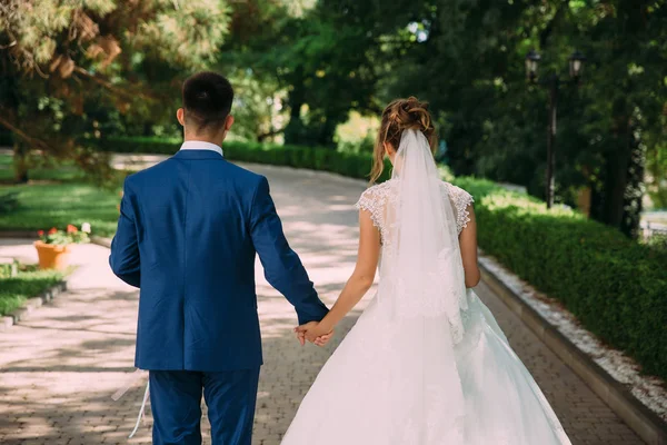 Een man en een vrouw houden handen en lopen in het park op hun trouwdag. Familie obligaties. — Stockfoto