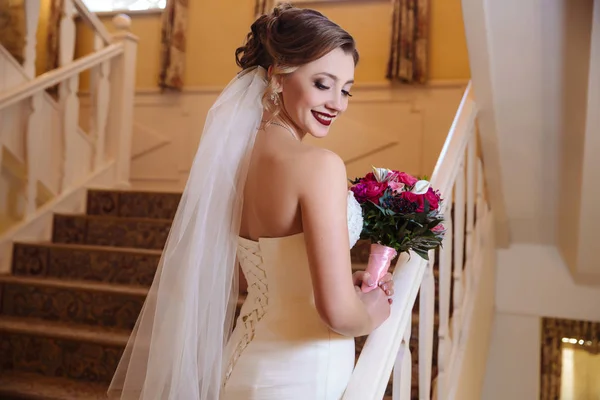 Vista da parte de trás de uma menina bonita em vestido de noiva branco posando em escadas e rindo . — Fotografia de Stock