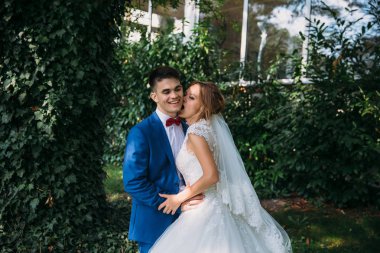 Güzel beyaz bir elbise içinde gelin Şakalar ve yanak üzerinde damat ısırıkları, adam silip süpürecek. Yeni evliler düğün gününde mutlu.
