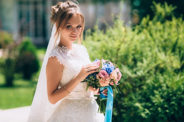 Güzel pembe-mavi buket çiçek ile yeşil bir bahçe içinde güzel bir yumuşak gelin yürür. Kız beyaz dantel gelinlik giyiyor, saçlarını toplanır, güneşe gülümsüyor ve bir