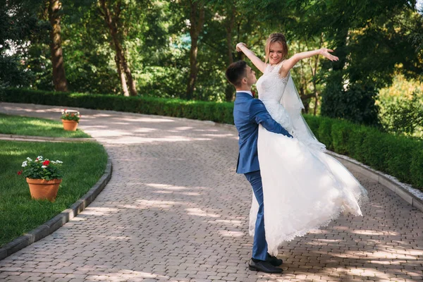 Um homem de fato clássico transforma a noiva. o cara levantou a menina em seus braços e adora olhar para ela, ela levantou as mãos para o céu e sorri, eles estão felizes . — Fotografia de Stock