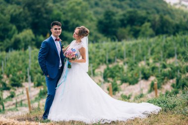 Mavi bir takım elbise ve Yeşiller arasında poz kar-beyaz uzun elbiseli gelin gelin. Kız güzel bir buket tutuyor onlar mutlular.