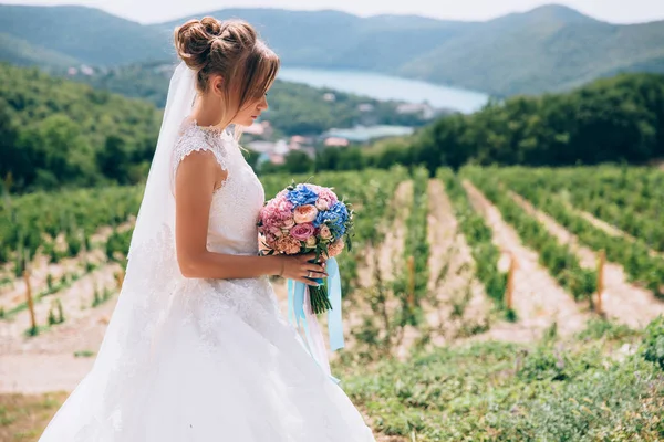 Bruden i profil på en bakgrund av vacker grönska och skyen beundrar henne bröllop bukett. — Stockfoto