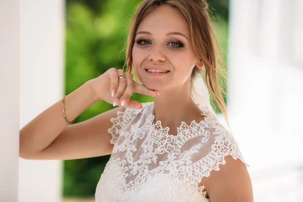 Blauäugige Blondine in einem mit Spitze bestickten Kleid posiert auf dem Foto. ein Mädchen blickt in die Kamera und lächelt mit der Hand am Kinn. — Stockfoto