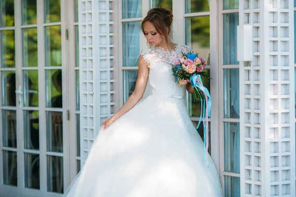 Bruden justerar tåget av sin klänning att gå in i hallen. Bröllop kläder, ser smink, smycken och blommor mycket vacker. — Stockfoto