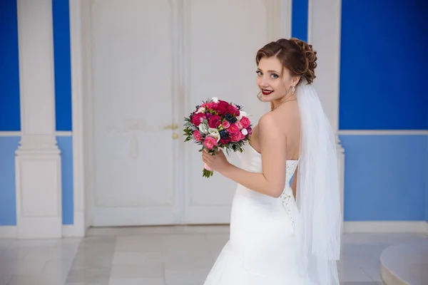 Θέα από το πίσω μέρος της νύφης χαμογελώντας γυρίζει γύρω μπροστά από την είσοδο στην αίθουσα της τελετής. Το κορίτσι μοιάζει πολύ χαρούμενος, δείχνει όμορφο ροζ μπουκέτο. — Φωτογραφία Αρχείου